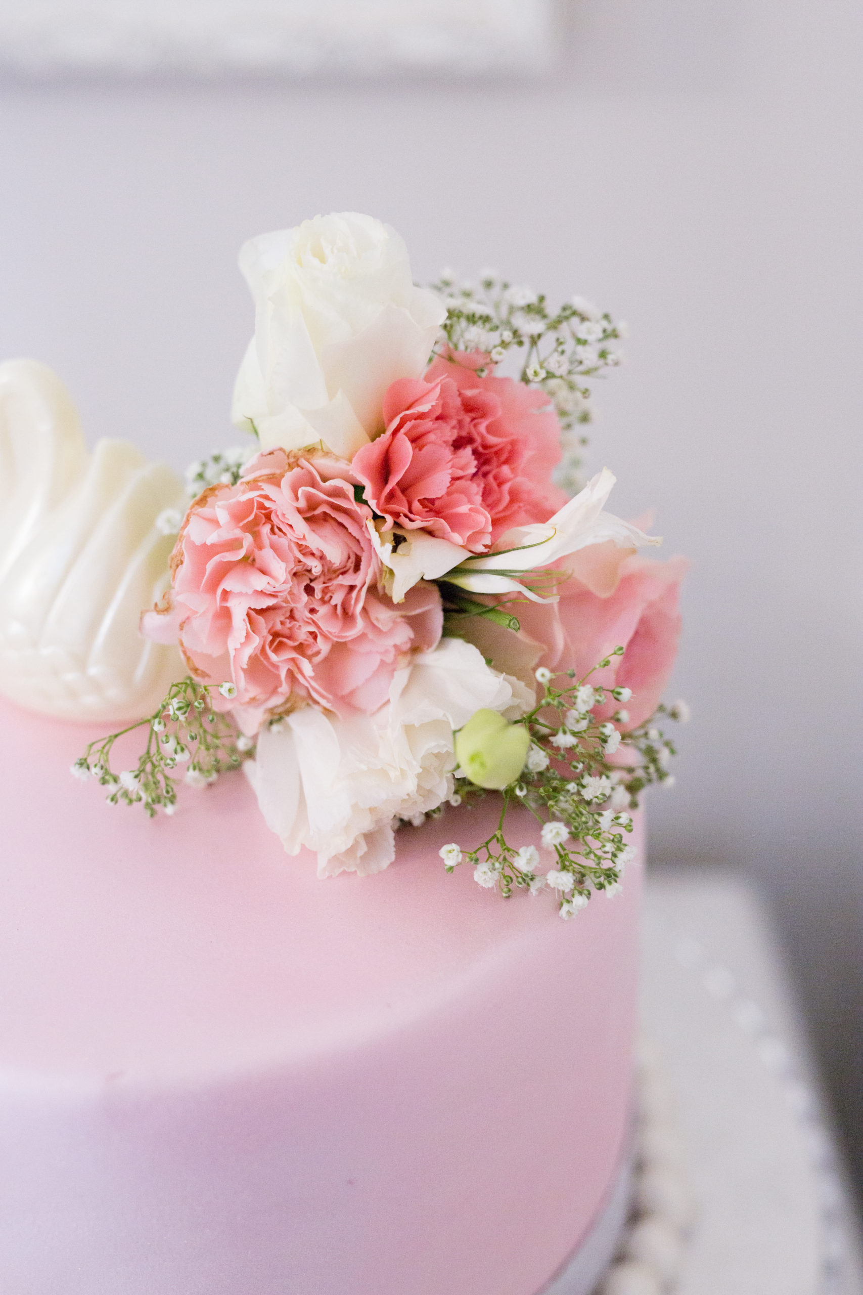 A pretty pink celebration cake with a white chocolate swan and  fresh flowers as decorations