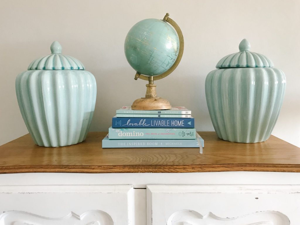 Blue home decor coffee table books arranged with aqua ginger jars and a globe