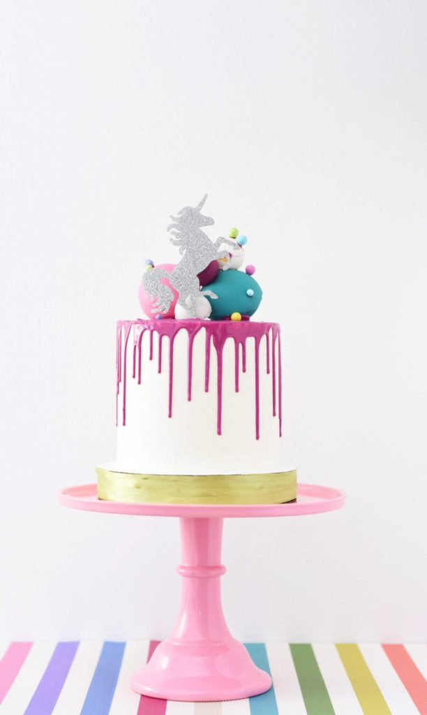 Unicorn birthday drip cake on candy striped table