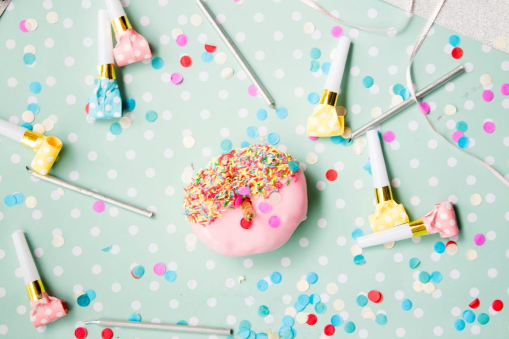 Pink donut on a turquoise background surrounded by party whistles